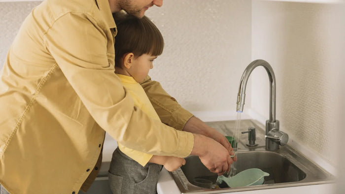 père qui lave la vaisselle de bébé